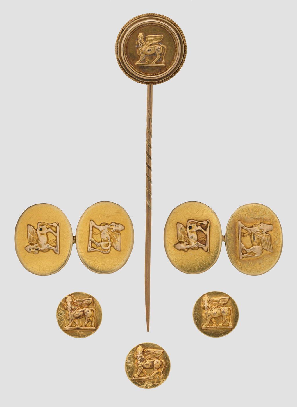 A matching group of gold men's jewellery - a stickpin, a pair of oval double-sided cufflinks and three round shirt studs - each decorated with a winged, human-headed bull in relief.